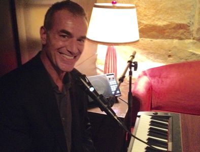Mike Petrone smiling at the microphone and sitting in front of portable keyboard.