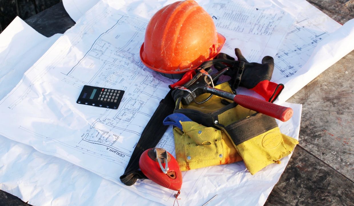 Construction tools and safety gear on building plans, representing practical building experience by St Clair Property Services.