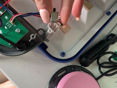 Hand holding a small electronic switch near a circuit board inside a device.