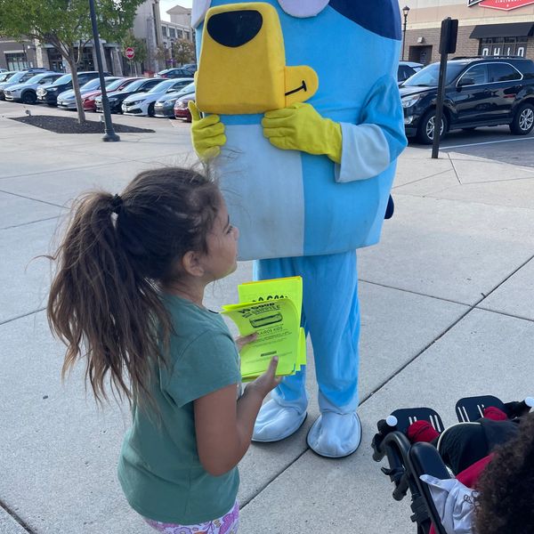 A girl interacts with a person in a blue cartoon mascot costume outdoors.