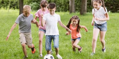 Five children joyfully playing soccer together on green grass.