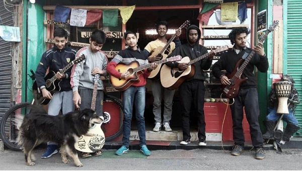 Group of young musicians with guitars and a dog on street.