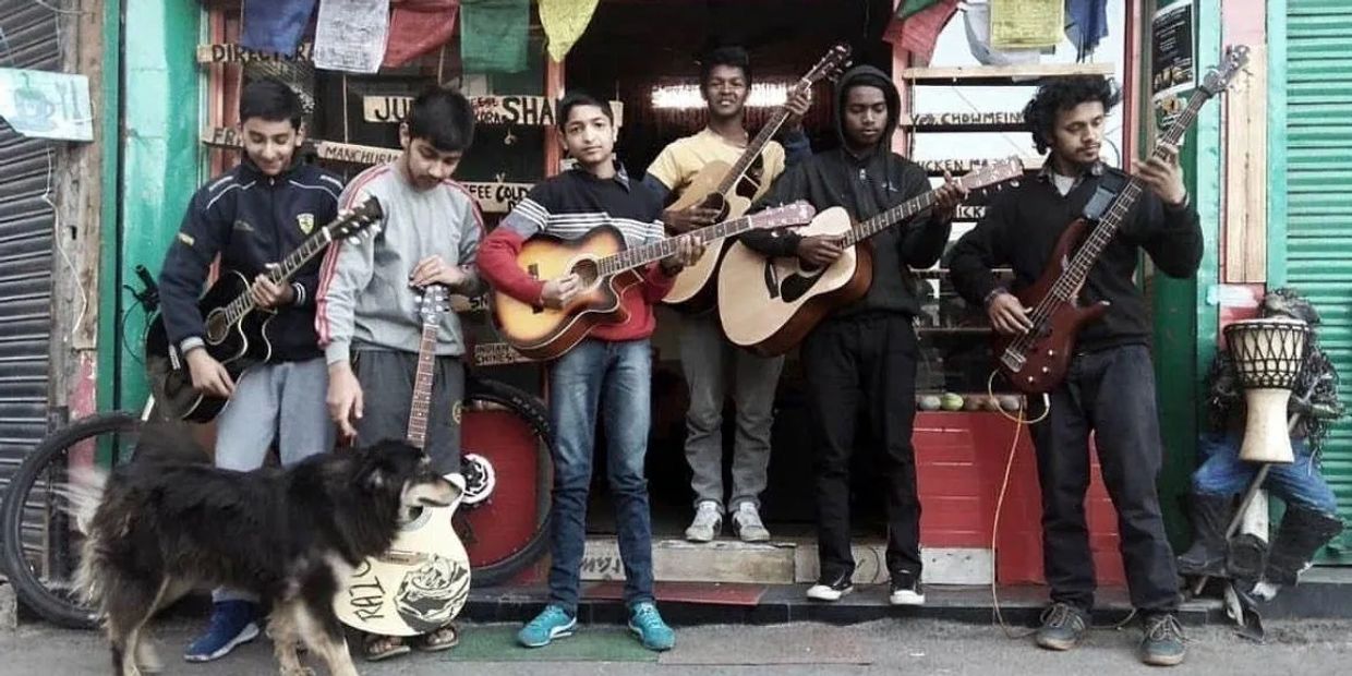Group of young musicians with guitars and a dog on street.