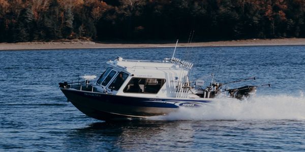A white fishing boat speeds across a lake with autumn trees in the background.