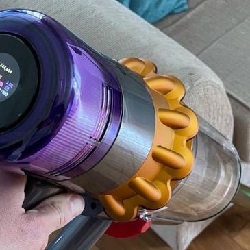 Handheld cordless vacuum cleaner with digital display in use near a sofa.
