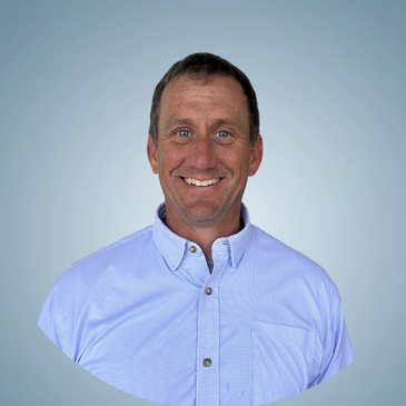 Smiling man in a light blue button-up shirt against a plain background.