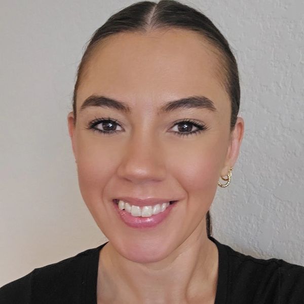 Smiling woman with neatly tied hair and gold hoop earrings.