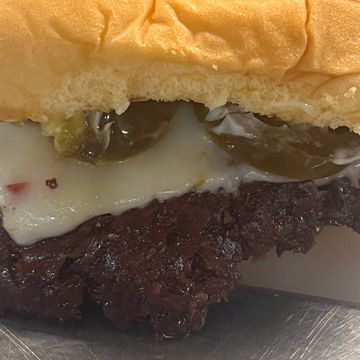 Close-up of a cheeseburger with jalapeños and melted cheese on a soft bun.