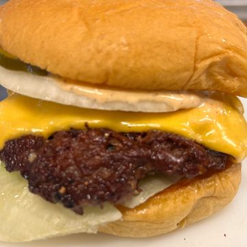 Close-up of a cheeseburger with melted cheese, onion, and lettuce.