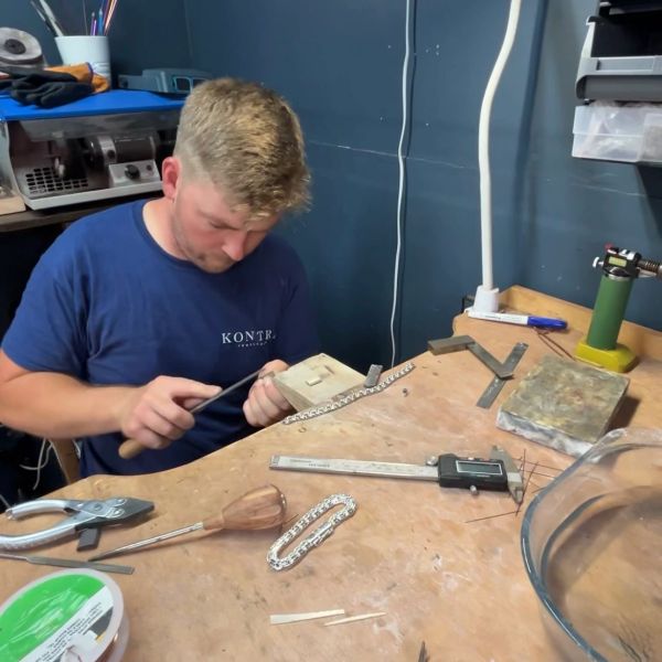 Man crafting jewelry with tools on a workbench.