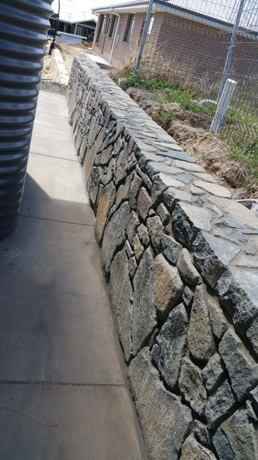 A stone retaining wall alongside a concrete pathway near a house.