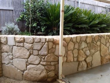 Stone retaining wall with green plants behind it under a covered patio.