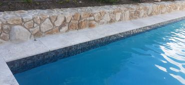 A swimming pool with blue water next to a stone wall.