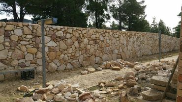A long stone wall under construction with scattered stones and metal posts.