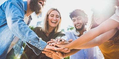 Group of diverse friends stacking hands in unity outdoors.