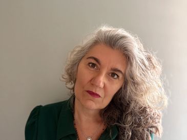 Woman with curly gray hair wearing a green blouse and necklaces.