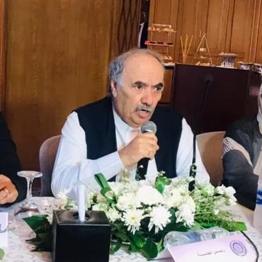A man speaks into a microphone at a decorated table during a formal meeting.