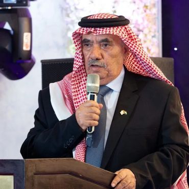 Man in traditional Middle Eastern attire speaking into a microphone at a podium.