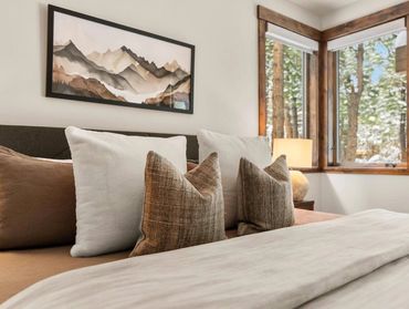 Cozy bedroom with earth-toned pillows and mountain artwork.