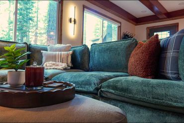 Cozy living room with plush blue-green sofa and decorative pillows near large windows.
