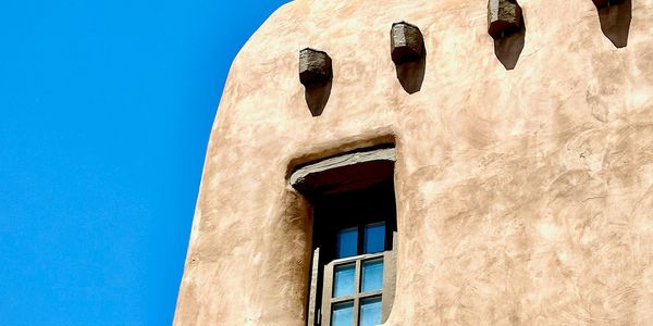 Adobe-style building wall with a small window under a clear blue sky.