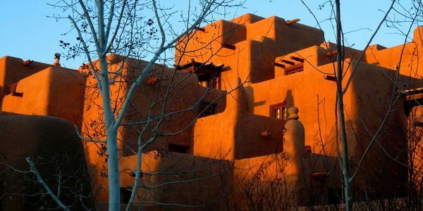 Adobe-style building glowing in sunset light with bare trees in front.