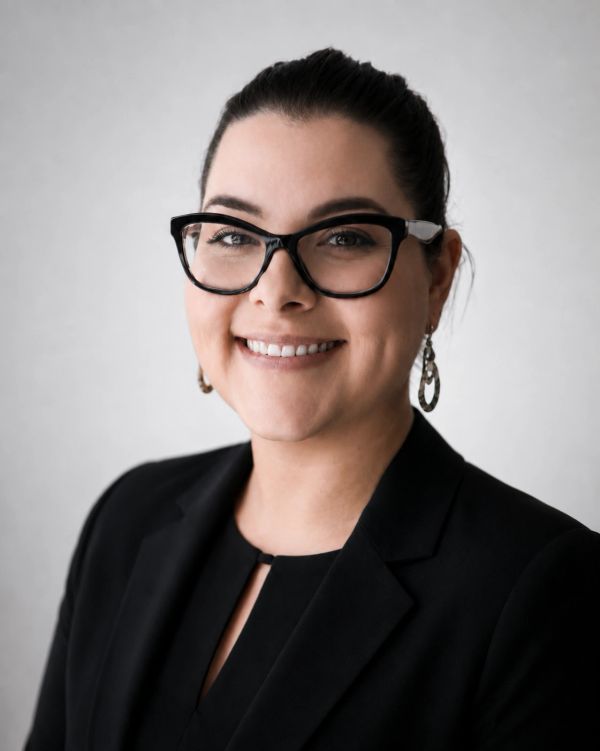 Professional woman wearing glasses and a black blazer smiling.