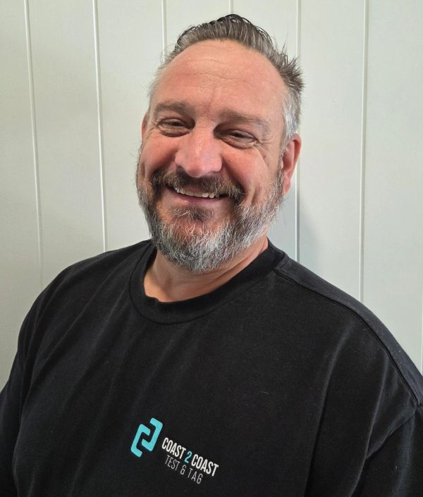 Smiling man with a beard wearing a black Coast 2 Coast Test & Tag shirt.