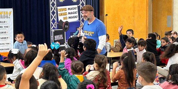 a group of students watch as school assembly performer magician Brian Scott interacts with the stude
