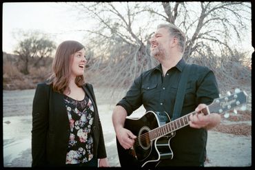 Male and female members of an acoustic cover band smile at each other in a wash near Tucson, AZ