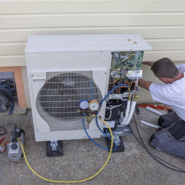 Technician servicing an outdoor air conditioning unit with tools and gauges.