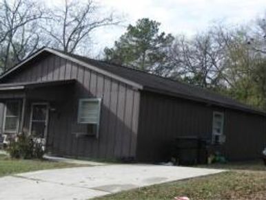 Small brown house with a slanted roof and driveway.