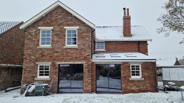 Snow-covered brick house with large windows and outdoor furniture.