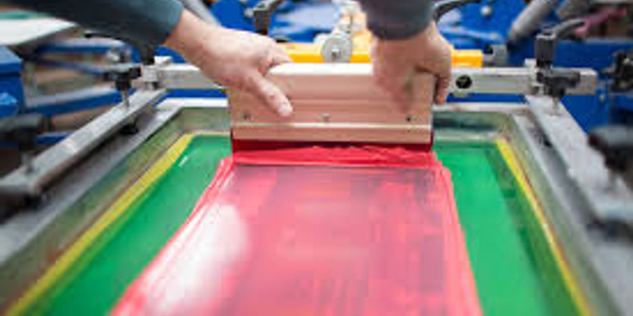 Hands applying red ink on a screen printing frame.