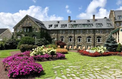 Historic stone building with colorful flower gardens under a blue sky.