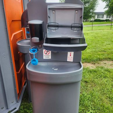 Portable handwashing station outside on grass near a portable toilet.