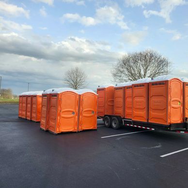 Orange portable toilets lined up in a parking lot on a trailer and on the ground.