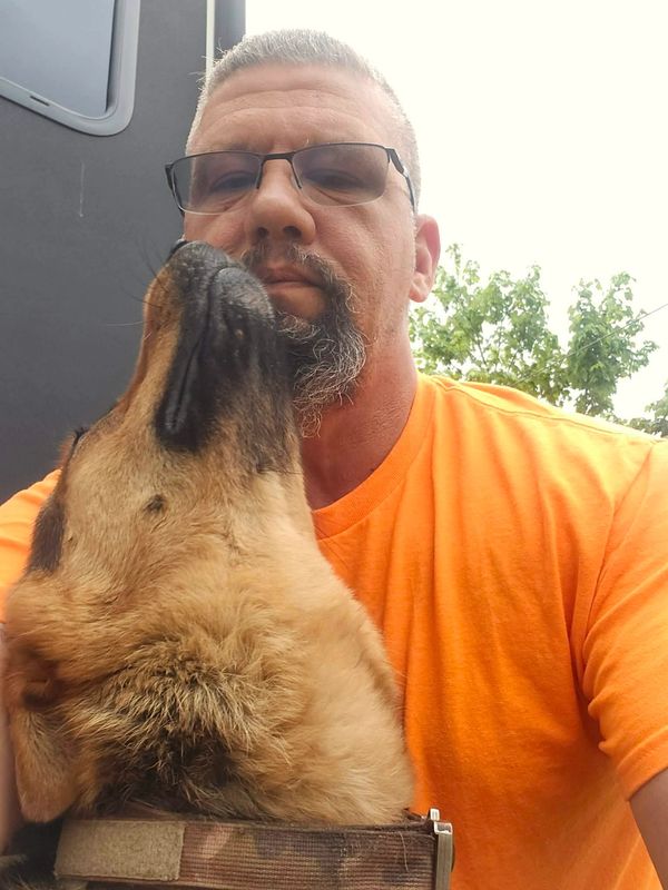 Man in orange shirt with glasses being affectionately nuzzled by a dog.