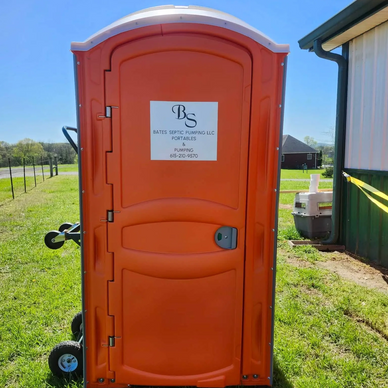 Orange portable toilet with company sign in a grassy area on a sunny day.