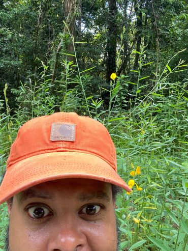 Man wearing an orange Carhartt cap in a green forest.
