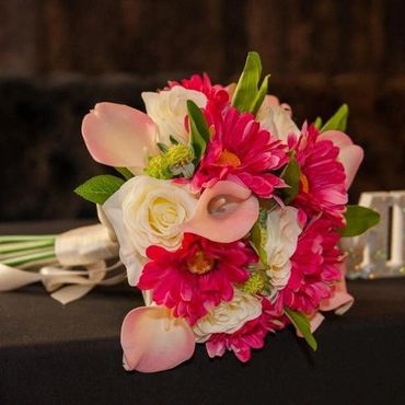 A colorful bouquet with white roses and bright pink flowers on a dark surface.