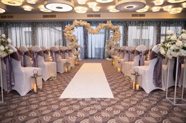 Elegant indoor wedding aisle with white chairs and floral heart arch.