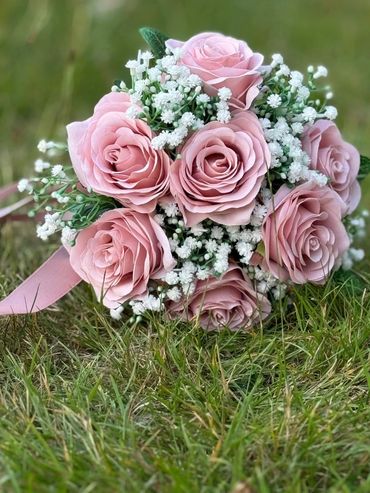 A bouquet of pink roses with white baby's breath on green grass.
