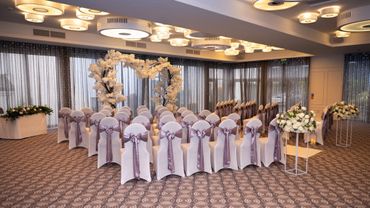Elegant indoor wedding setup with white chairs and floral decorations.