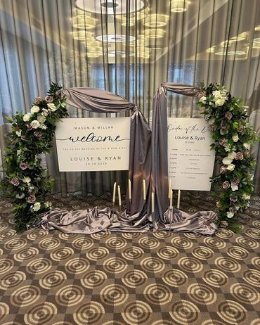 Elegant wedding welcome and schedule signs adorned with flowers and satin fabric.