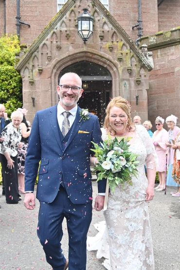 A joyful bride and groom walking with petals falling around them after their wedding ceremony.