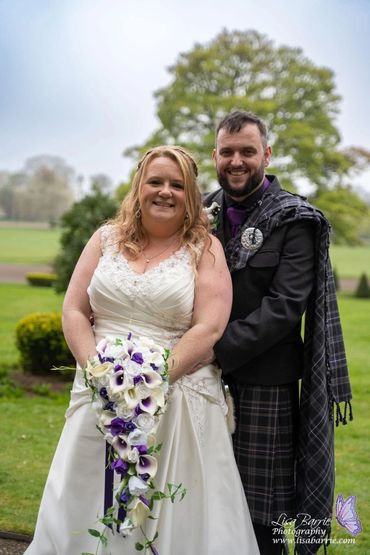 Happy couple on their wedding day, the groom in a kilt and the bride holding a cascading bouquet.