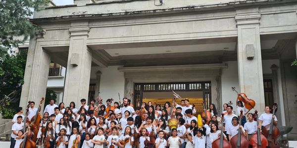 A large group of young musicians holding string instruments on steps of a classical building.