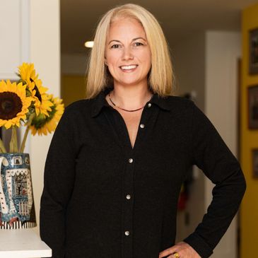 Alexis smiling at the camera wearing a black button down shirt dress with a necklace and yellow sunf