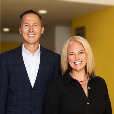 Gerald and Alexis smiling at the camera. Gerald with a dark blue suit jacket and white shirt. Alexis